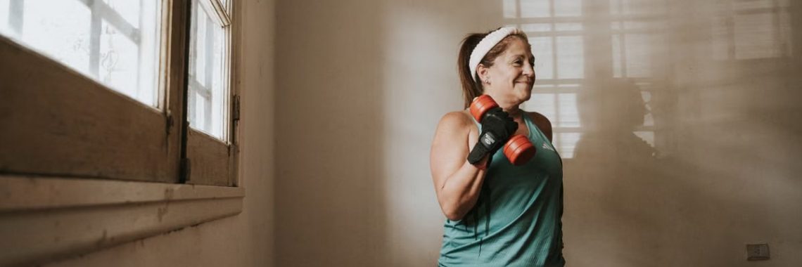 A woman lifting dumbbells indoors by a window, focused on her workout routine.
