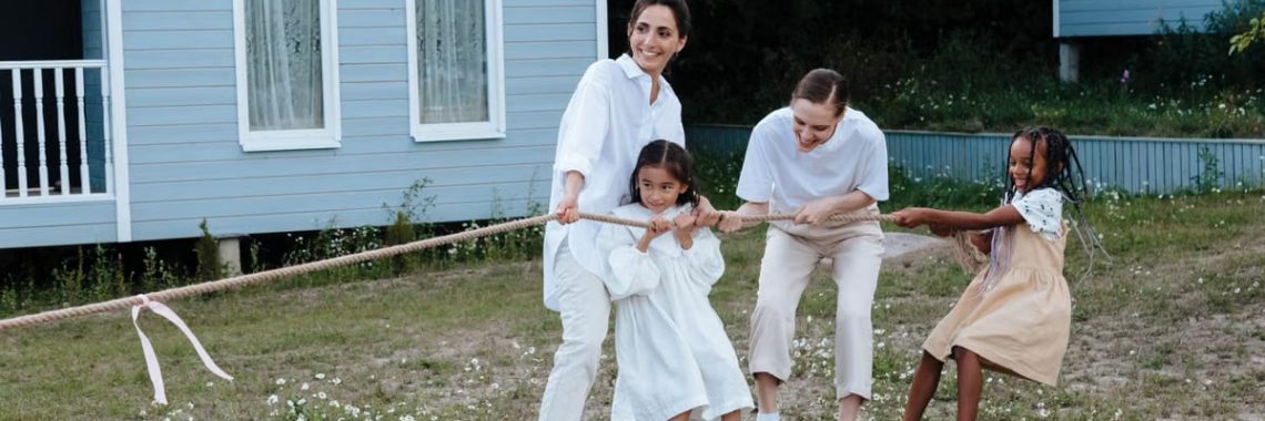 A happy family enjoys a game of tug of war in a grassy field by a house.